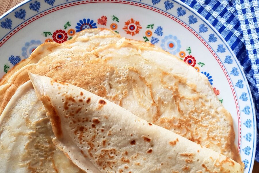 Een stapel pannenkoeken van bovenaf op een bord. Het bord staat op tafel met een geruit tafelkleed.